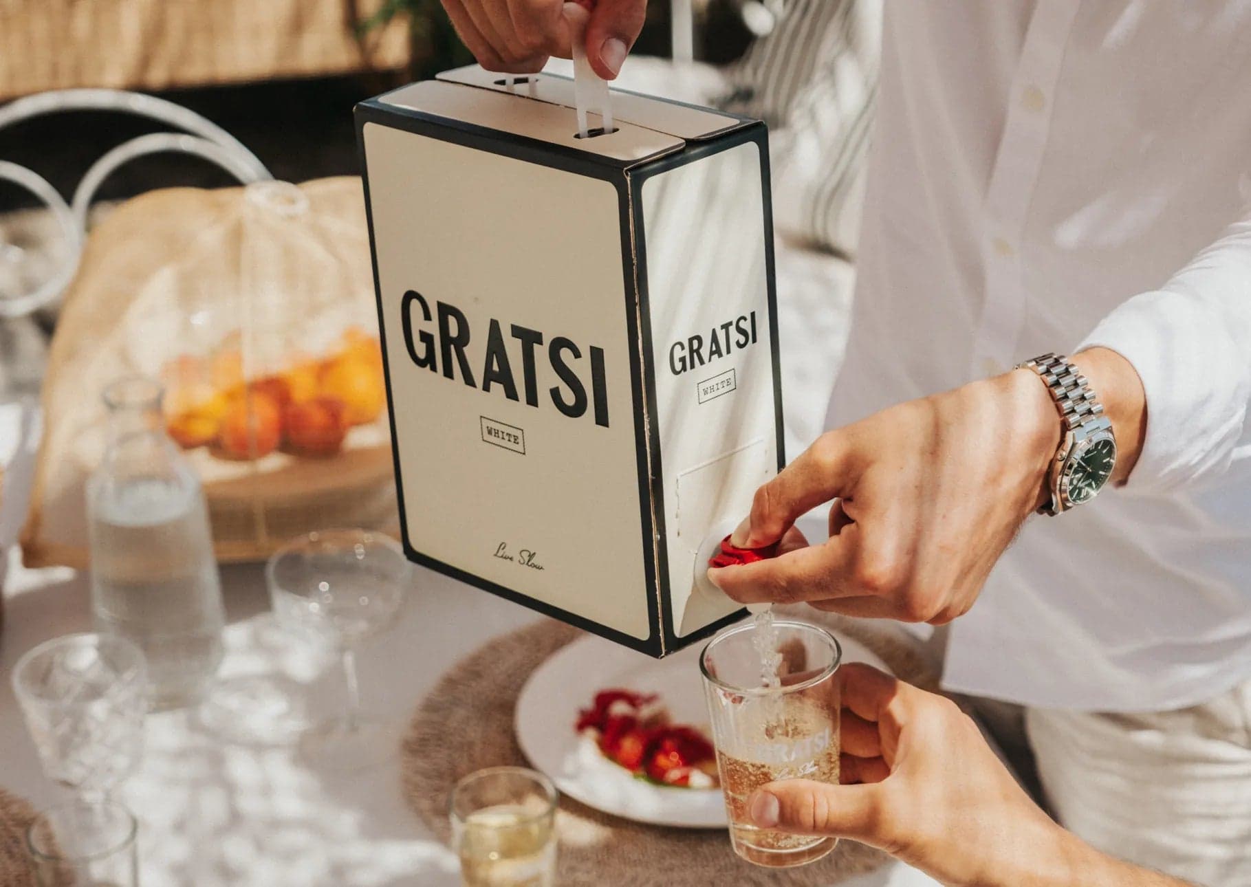 A person pours Gratsi White into a glass at a dining table